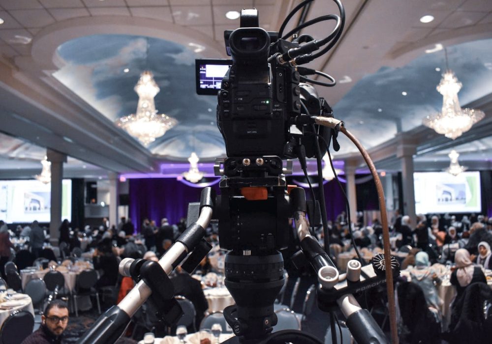 camera facing stage in ballroom of large corporate event